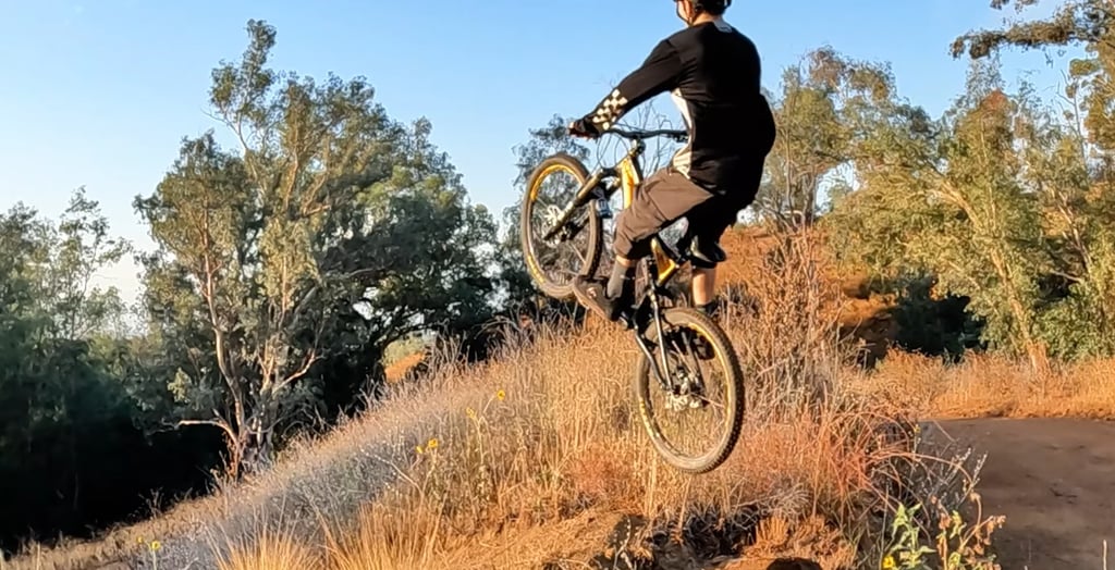 Mountain biker leaning too far back mid-air, about to land rear wheel first on a dirt jump — risk of