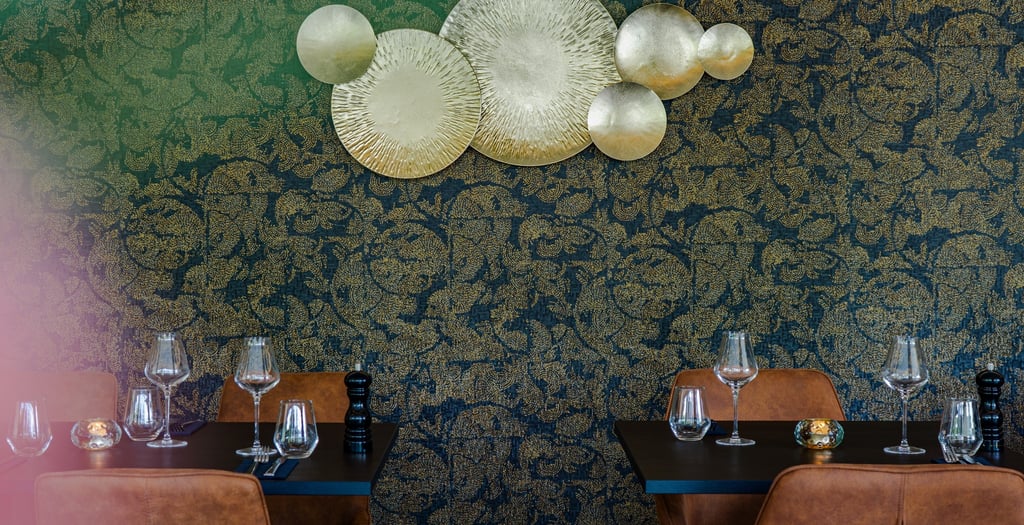 Elegant gedeckte Restauranttische mit Weingläsern vor gold-schwarzer Blumentapete