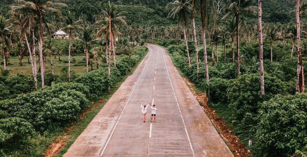 two people walking down a road with palm trees