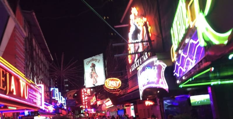 Leuchtende Neonschilder in der belebten Nachtleben-Straße Soi Cowboy in Bangkok.