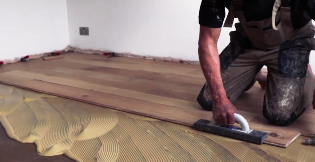 Professional installer installing hardwood flooring using glue down method.