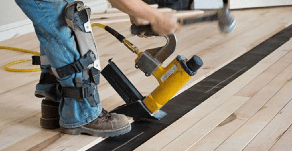 Professional installer is installing hardwood flooring with a nail gun.