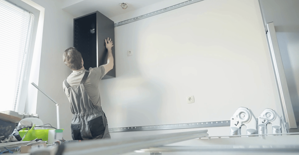 Mężczyzna montuje korpus szafki wiszącej za pomocą listwy montażowej 