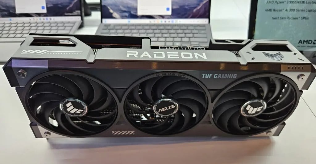 placa de video radeon encima de una mesa , se ve atras 2 notebooks encendidas