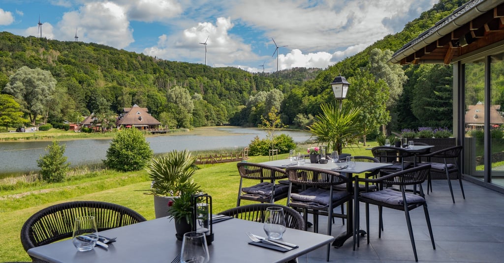 Außenterrasse eines Restaurants mit Blick auf See, grüne Hügel und Windkraftanlagen