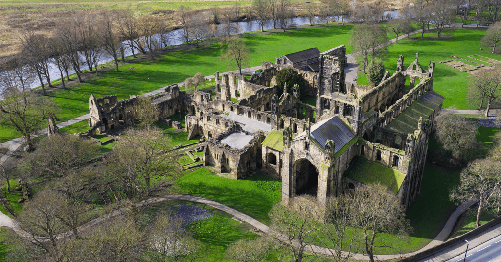 Aerial view of Kirkstall Abbey ruins in Leeds surrounded by green parkland and the River Aire.