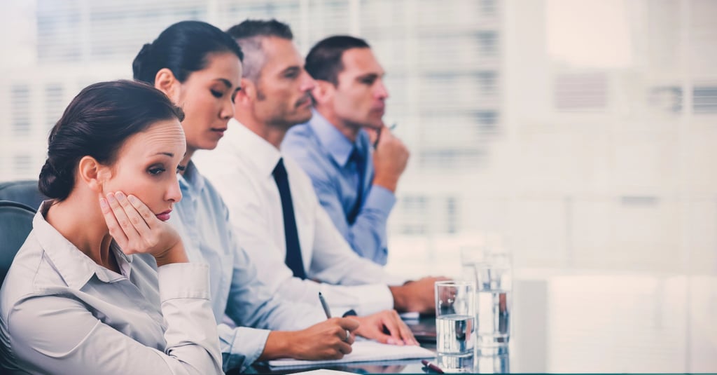 Bored business professionals attending a corporate meeting in a modern office boardroom.