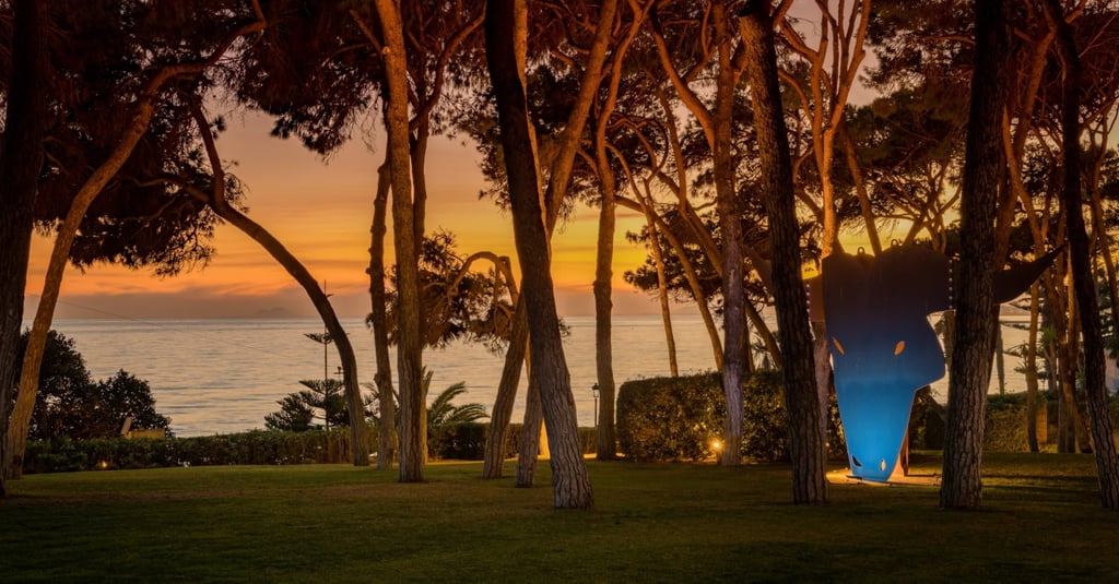 Seafront garden at dusk with illuminated sculpture and pine trees