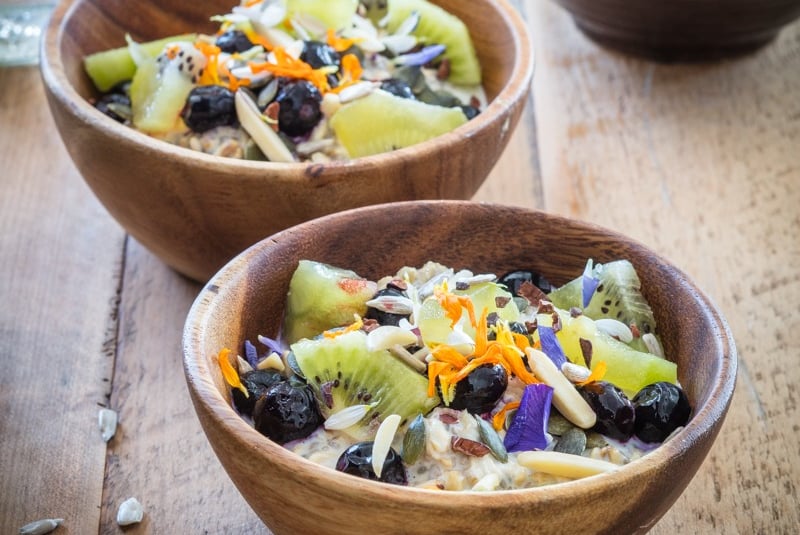 two wooden bowls of oaty chia coconut with fruit and nuts on a table