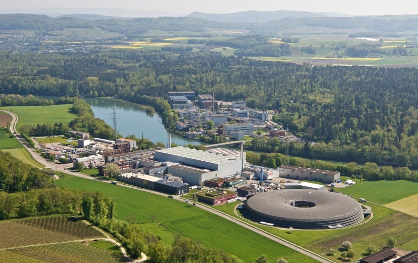 Aerial view of Paul Scherrer Institute complex with verdant landscape, lake, and forested hills