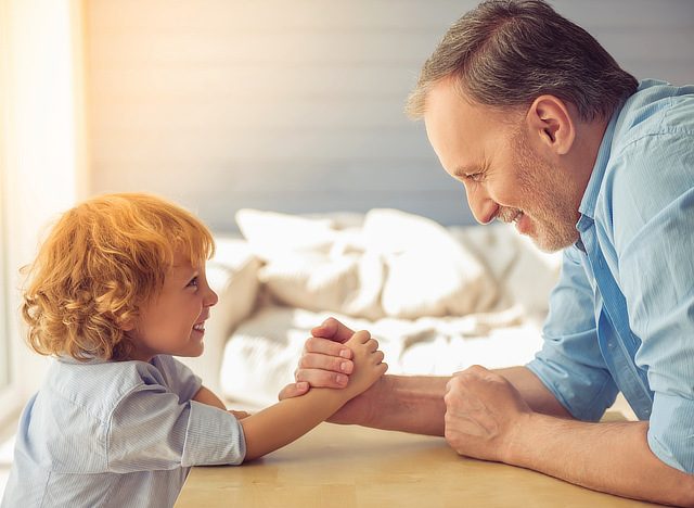 father and son arm wrestling and laughing - language science - who learns better