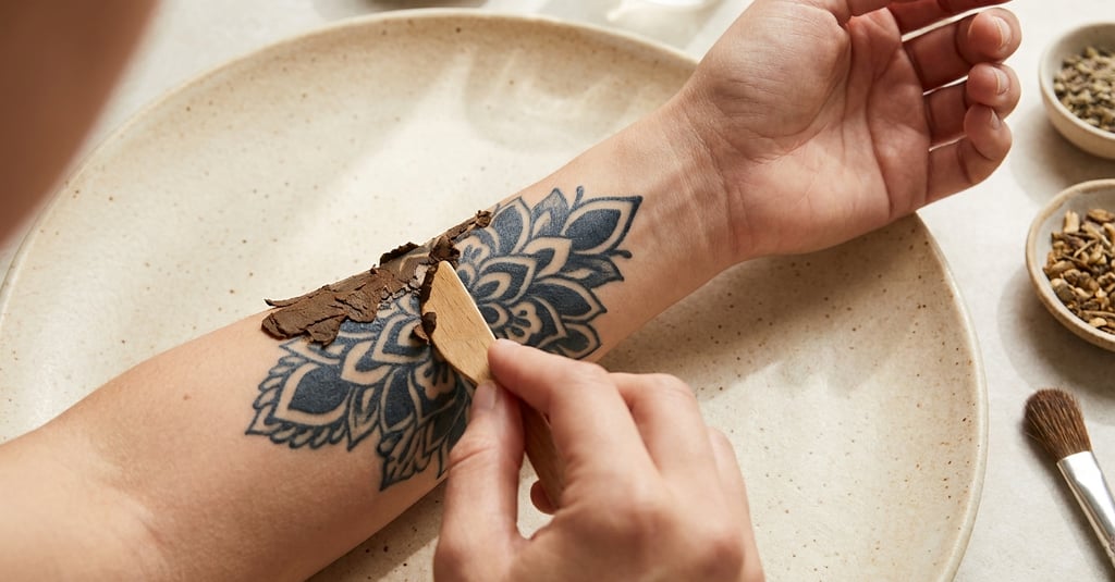 Applying a natural herbal paste over a mandala tattoo with a wooden spatula for skin care.