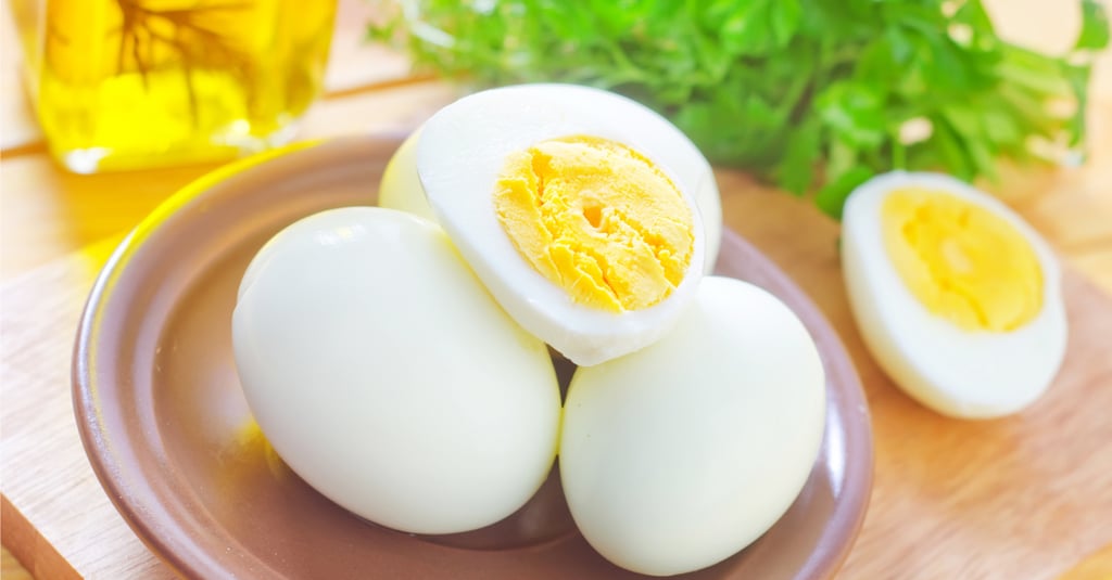 Hard-boiled eggs peeled and halved on a plate with fresh parsley and olive oil in the background.
