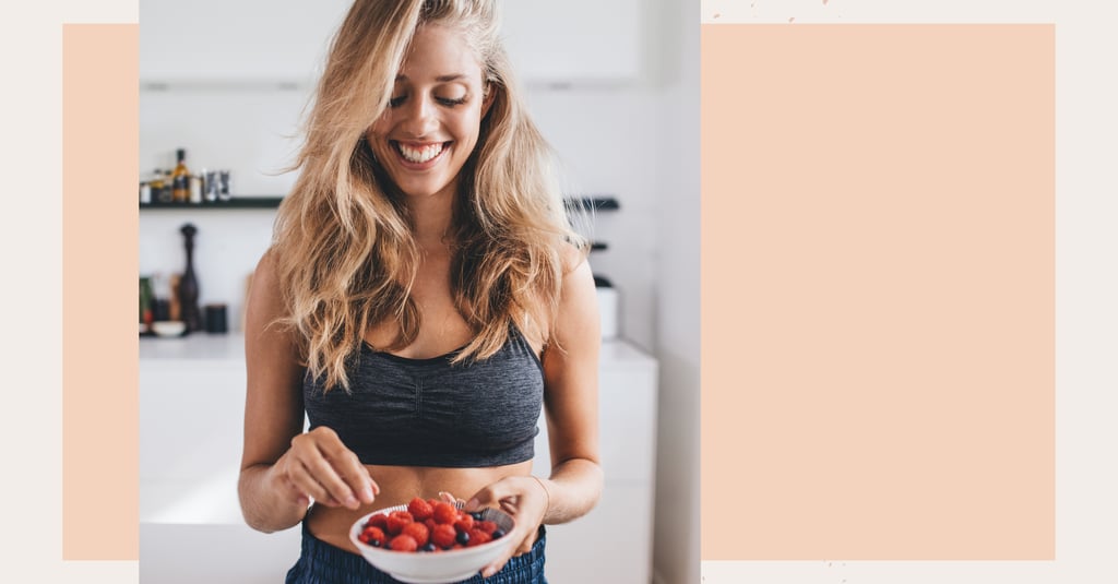 Smiling woman in fitness wear holding a bowl of fresh raspberries and blueberries.
