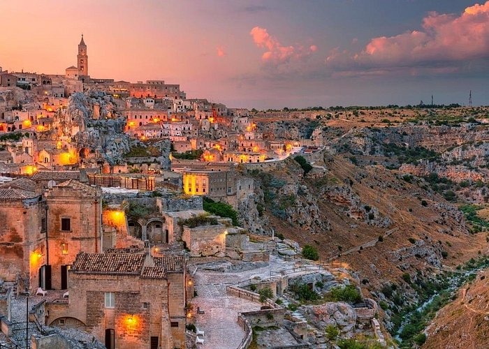 A panoramic view of Matera's ancient Sassi district at sunset with glowing lights and stone architecture.