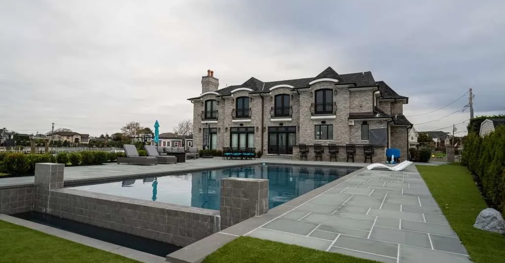 Luxury backyard with a modern geometric pool, stone patio, and a grand grey brick mansion.
