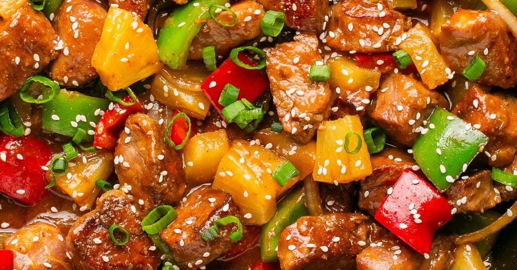 A plate of Sweet and Sour Pork with colorful bell peppers and pineapple chunks, served with steamed 