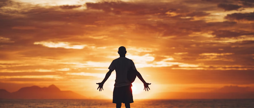 A person stands with open arms at sunset, expressing wonder, surrender, and spiritual searching.