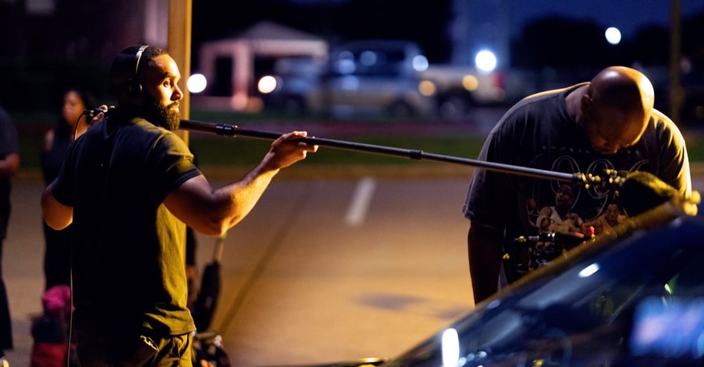 a man holding a boom pole next to the director of photography on a scripted narrative set