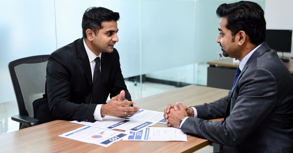 Two male professionals in suits having a business meeting or job interview at an office desk.