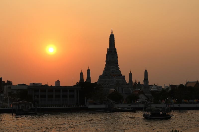 Silhouette des Wat Arun vor einem leuchtend orangefarbenen Sonnenuntergang über dem Chao-Phraya-Flus
