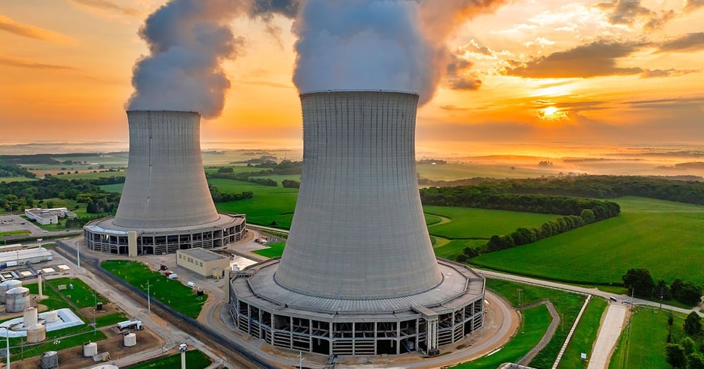 Aerial view of a nuclear power plant with two cooling towers emitting steam during a vibrant sunset.