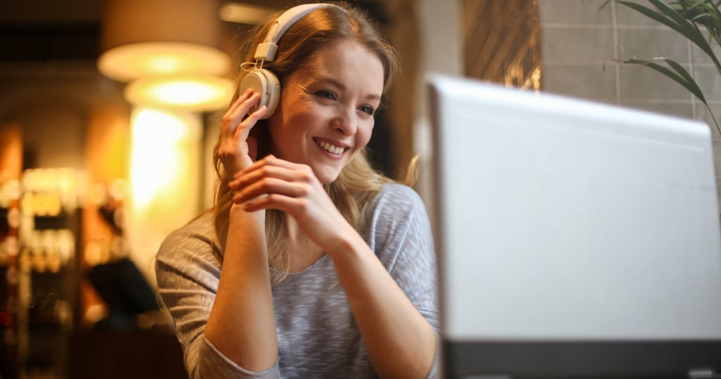 a woman in a gray sweater and headphones on a laptop