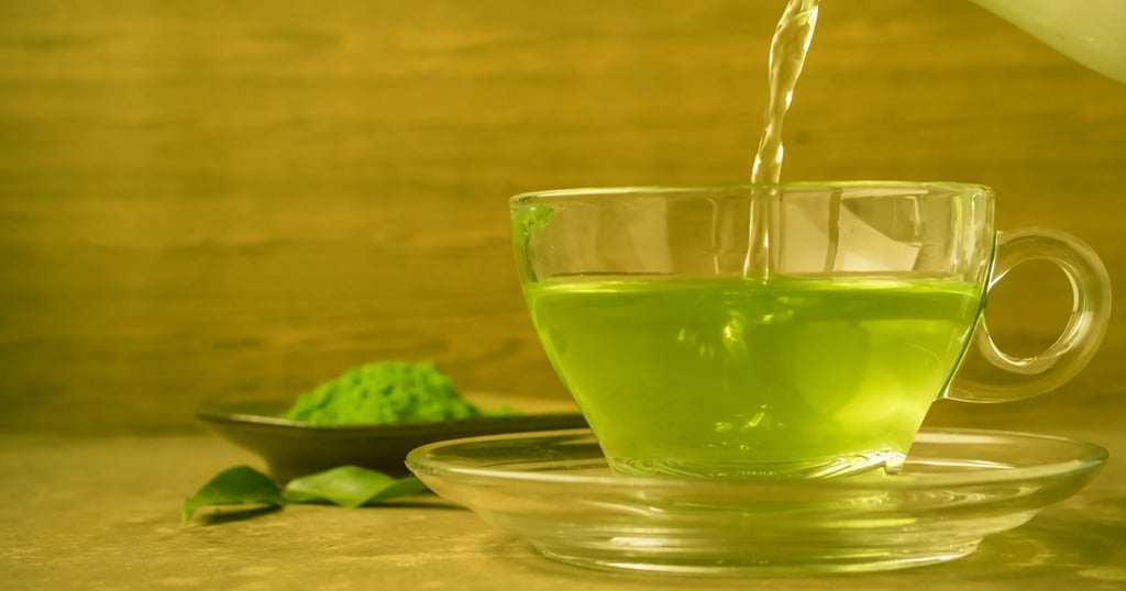 Té verde vertiéndose en una tasa de crista, con polvo de te matcha y hojas de té verde