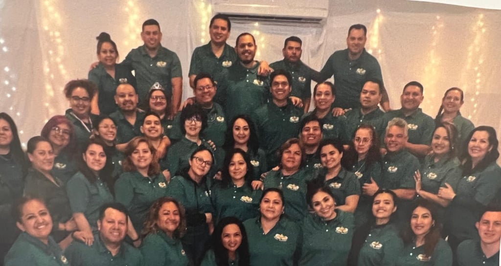 A large diverse group of professional team members posing for a corporate staff photo wearing green polo shirts.