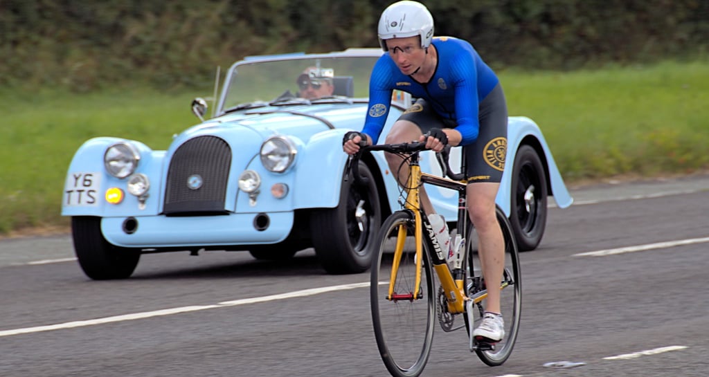 a man riding a bike with a car behind him