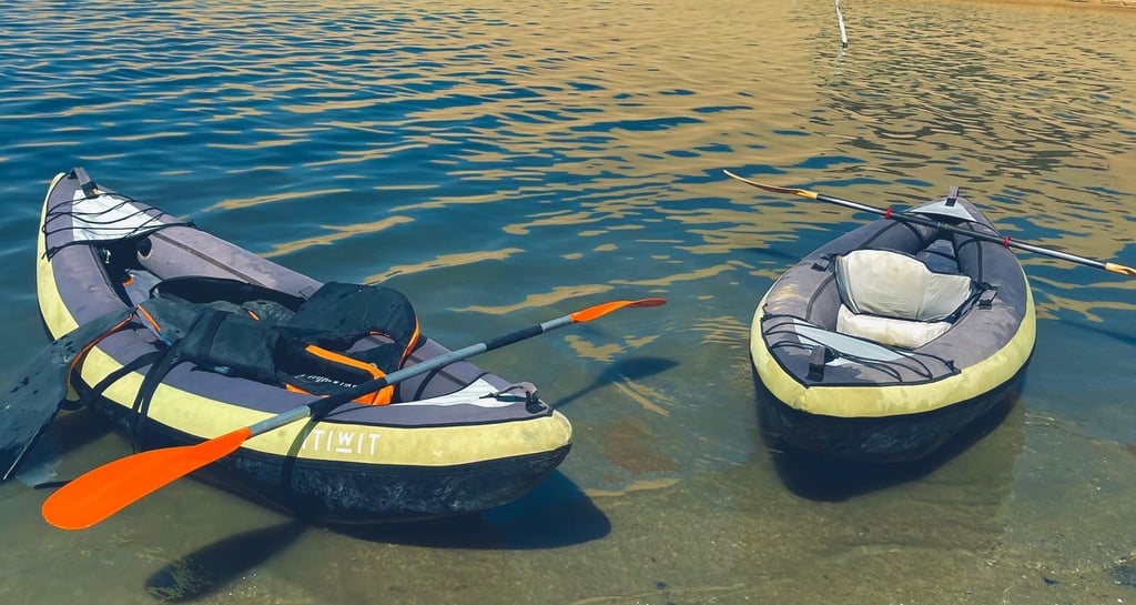 Two inflatable kayaks with paddles rest in the shallow water of a lake. 