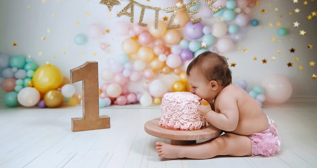 Baby girl celebrating a first birthday cake smash with pink frosting and pastel balloon backdrop.