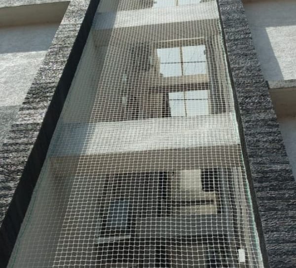 Evening view of a balcony fully protected by pigeon netting, with city lights in the background.