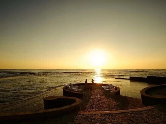 a person sitting on a bench in front of the sun