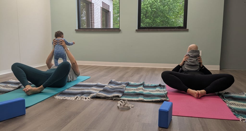 Two mothers laying on two yoga mats. Both are holding their infants.