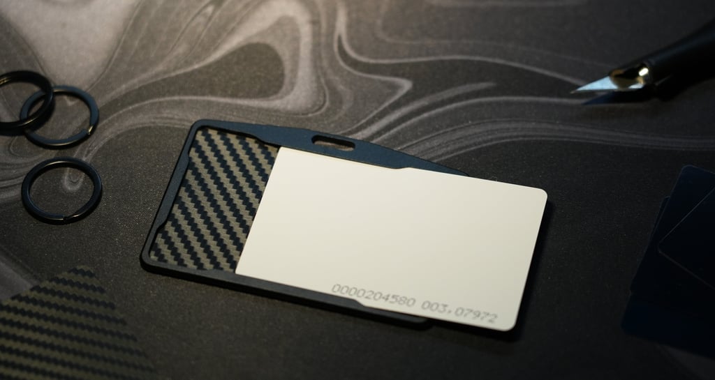 A carbon fiber ID badge holder with a blank white plastic card on a dark marble desk.