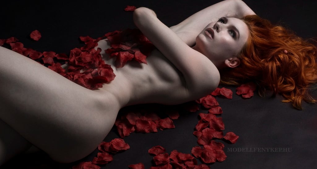 a beautiful youngwoman with red hair covered with red rose petals implied nude glamour