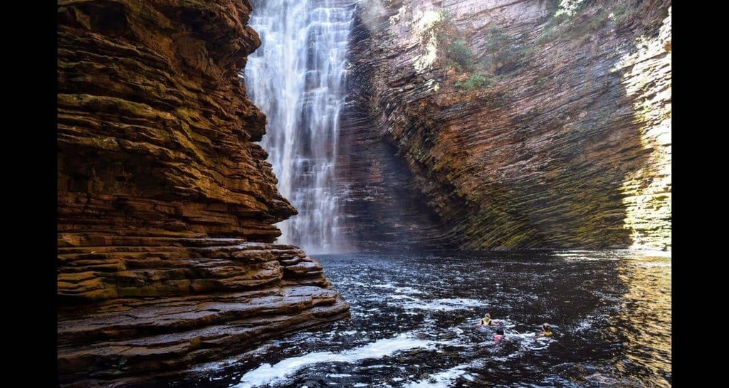 a person swimming in a river near a waterfall