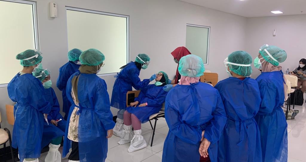 Tim medis mengenakan APD biru sedang bersiap dan berdiskusi di ruang isolasi rumah sakit
