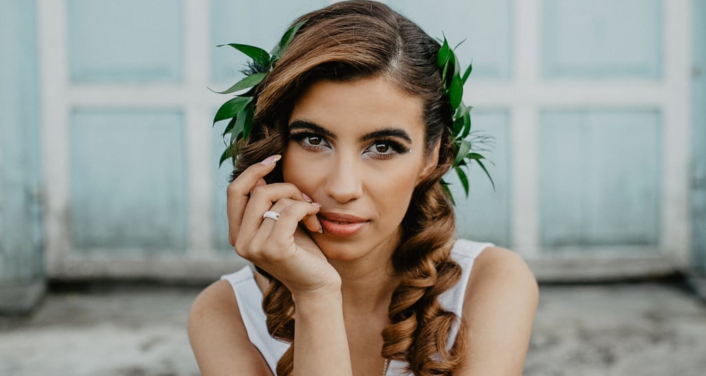 Portrait of a bride with curly hair and a green leaf headpiece in front of a blue door.