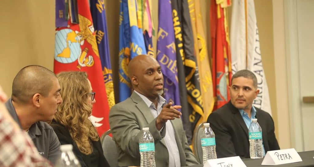 Lee Jones in a suit and tie is sitting at a table with a microphone