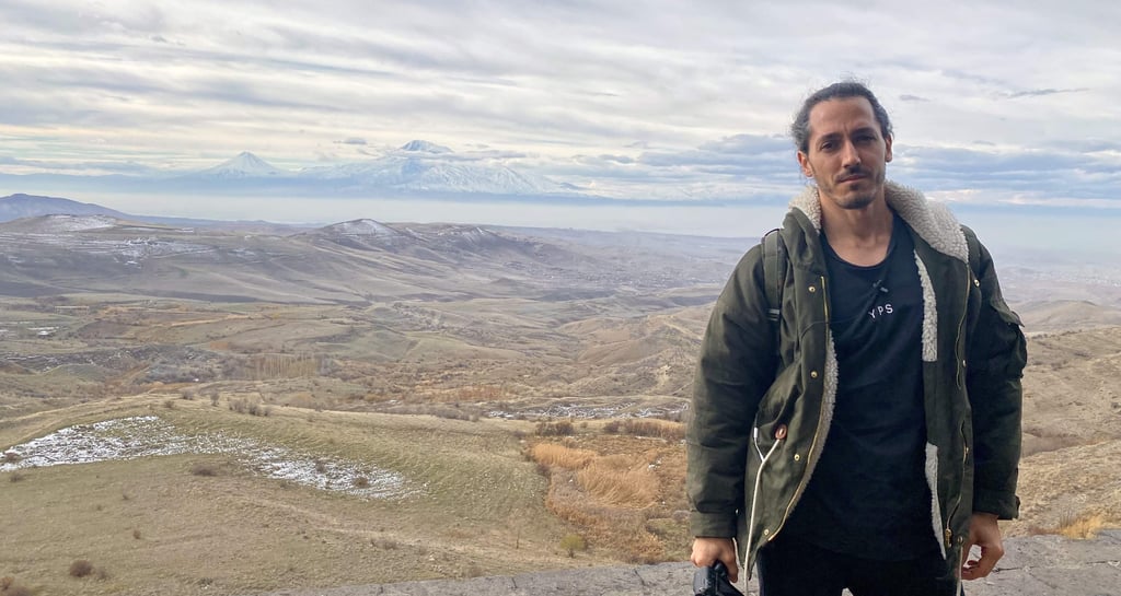 Persona posando con el monte Ararat al fondo en Armenia, paisaje montañoso y cielo nublado