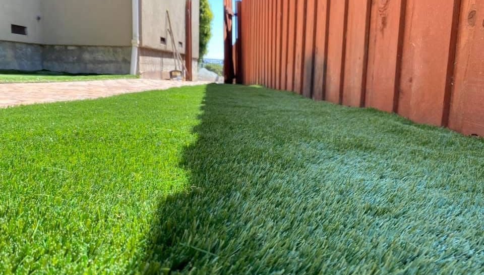 Freshly installed green artificial grass turf in a residential backyard next to a wooden fence.