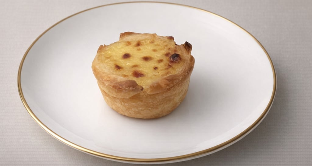 Golden Portuguese custard tart with caramelized top on a white gold-rimmed plate.