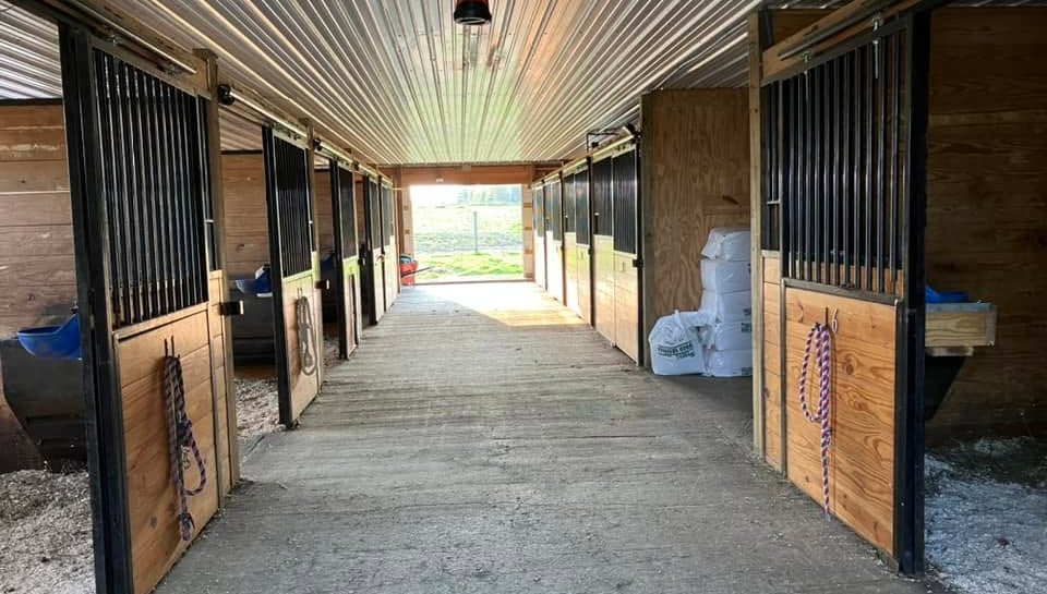 Interior view of a clean horse barn with wooden stalls and a concrete aisle way.