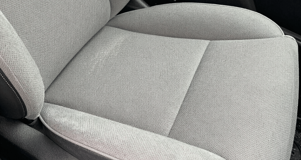Close-up of a leather car seat before deep cleaning, showing stains and wear.