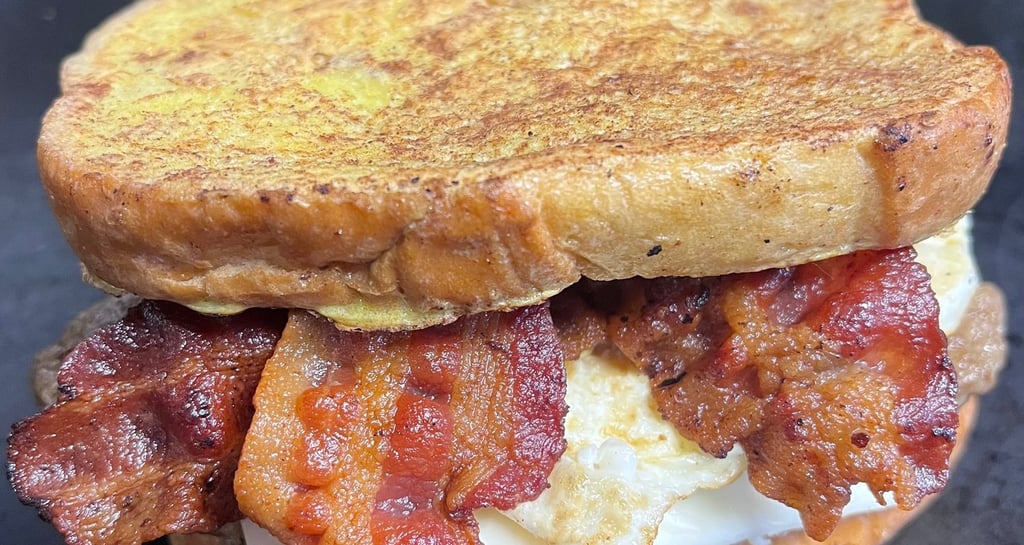 Hearty bacon breakfast sandwich loaded with crispy bacon, scrambled eggs, and melted cheddar on toasted bread—Slap Yo Self’s 