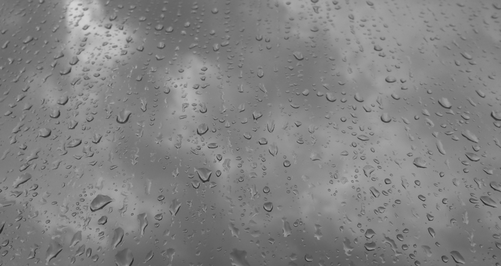 Gotas de lluvia sobre un cristal en blanco y negro con cielo nublado.