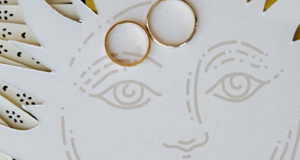 Two gold wedding bands resting on a white sun illustration with a yellow background.