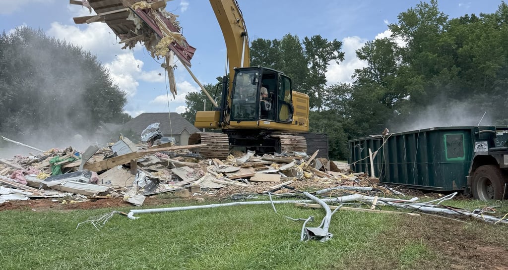 Excavator loading demolition debris in dumpster
